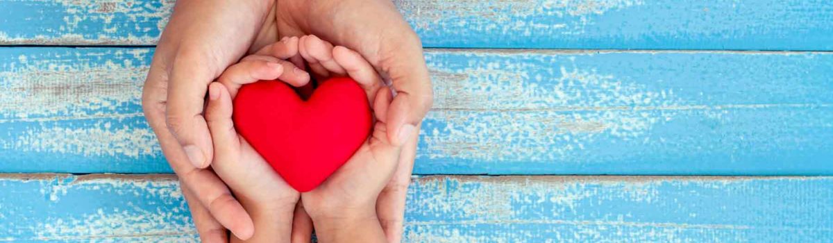 adult and child hands holding a red heart